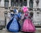 Two beautiful women holding fans and wearing hand painted masks and ornate blue and pink costumes at Venice Carnival
