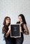 Two beautiful women holding a felt letter board with the words Love Is Here on white brick wall background