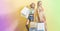 Two beautiful women stand against multi-colored wall holding shopping bags in their hands. Satisfied shopaholics.