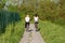 Two beautiful young girls in sport outfit riding their bicycles on paved country path surrounded with high green grass and forest