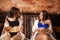 Two beautiful young girls in swimsuits lay on wooden lounger in the sauna are discussing the news while looking into the phone