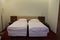 Two beds with thick mattresses with white linens on the floor red carpet and light walls