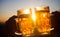 Two beer glasses in hands against blue sky and sun in the evening. Outdoor party, picnic concept