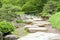 Two benches, green plants, flowers, stone road and lake in garden