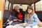 Two best interracial girlfriends sitting in wide open trunk of old vintage minivan car reading books