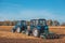 Two big blue tractor plowing a field and remove the remains of previously mown corn.