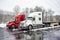 Two big rig long haul semi truck tractors with flat bed semi trailers standing side by side on the winter wet truck stop with snow