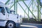 Two big rigs semi trucks running side by side on the road on the green truss bridge