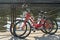 Two bikes white and red of travelling together persons parked and locked with anti-theft cables to the fence