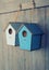 Two birdhouses hang on with wood background.