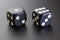 Two black dice close-up on a dark illuminated surface