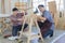 Two black hair asian adult carpenters wearing plaid shirt smiling happily assemble wooden desk together by using electric