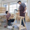 Two black hair asian adult carpenters wearing plaid shirt smiling happily assemble wooden desk together by using electric