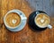 Two black and white cappuccino cups with art heart shape on brown wood table top view