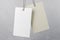 Two blank eco hanging tags: empty white and beige made from recycled kraft paper at grey wall background. Recycle eco label tag