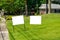 Two blank white signs on a green grassy lawn in a residential community