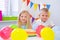 Two blonde caucasian kids boy and girl in birthday hats looking at camera and smiling at birthday party. Colorful