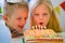 Two blonde caucasian kids boy and girl have fun blowing out candles at birthday rainbow cake with burning candles at