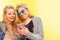 Two blonde students friends laughing using mobile phone in a yellow wall