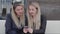 Two blondes are sitting in a cafÃ© and discuss photos in the smartphone