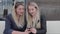 Two blondes are sitting in a cafÃ© and discuss photos in the smartphone