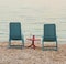 Two blue chairs with a red table in the middle standing on the pebble beach of the Adriatic Sea in summer on a warm evening