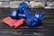 Two blue hand weights beside a red elastic exercise band against wooden background