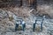 Two blue plastic chairs with frozen rime in a rural garden with rustic farm house and grass covered in ice cold hoar