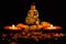 Two blurred clay lamps on rose petals in front of buddha statue against black background. religious concept