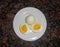 Two boiled eggs on a white plate, one in halves. showing yolk. Dark granite background. Overhead