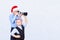 Two boys in caps of Santa Claus are photographing on a light background