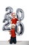 Two boys in Christmas hats are holding silver inflatable figure 2020. White background. New year concept