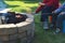 Two boys are grilling or barbecuing Polish sausages over an open fire pit in their backyard