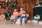 Two boys in identical clothes sit under Christmas tree with gifts