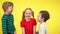 Two boys kissing pretty little girl at yellow background. Portrait of playful smiling children having fun. Brothers and
