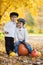 Two boys in the park, sitting on a big pumpkin, smiling