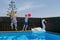 Two boys play with a ball and jump into a blue water pool.