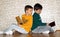 Two boys are reading books,one turns and looks at the other volume