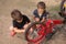 Two boys are repairing a red bike outdoors, holding tools, a lifestyle