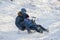 Two boys ride on sleds, descend from a snowy mountain and brake with their feet