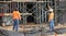 Two brick masons stand in front of scaffolding discussing the installation of brick veneer on a new building