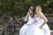 Two brides pose on wooden bench in forest with mountain bikes ne