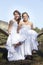 Two brides in white dresses pose on hammock in forest on sunny s