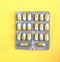 Two bright blisters of white and orange capsules. Pills on a light yellow background. Painkillers, drugs, antibiotics.