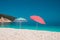 Two bright colored sun beach umbrella on pebble beach against turquoise blue sea water surface and clean blue sky