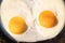 Two bright round raw yolks in finish white with edge cracks in a dark skillet. Cooked small fried eggs is a simple breakfast.