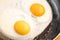 Two bright round raw yolks in whites with edge cracks in a frying pan. Cooked tender, soft fried eggs is a simple dish.