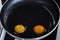 Two bright round yolks with raw whites, uncooked small fried eggs is a simple breakfast in a black skillet. Top view, close-up,