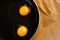 Two bright round yolks in transparent whites in a black frying pan on a paper. The concept of the process of cooking a simple dish