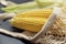 Two bright yellow peeled corn on cob on a black background in white shopping net with husk